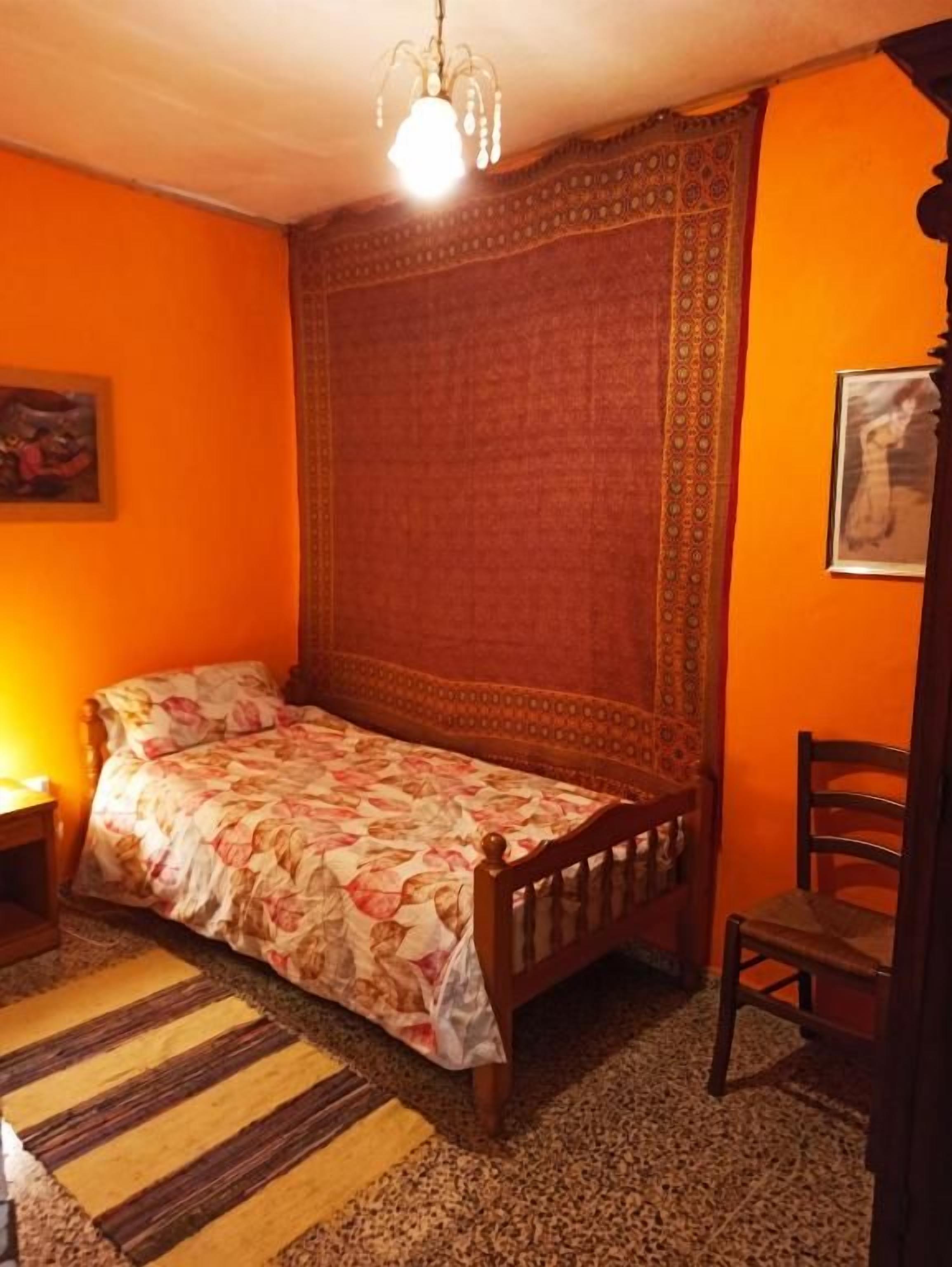 Una habitación con cama, una silla, un tapete y una araña.
