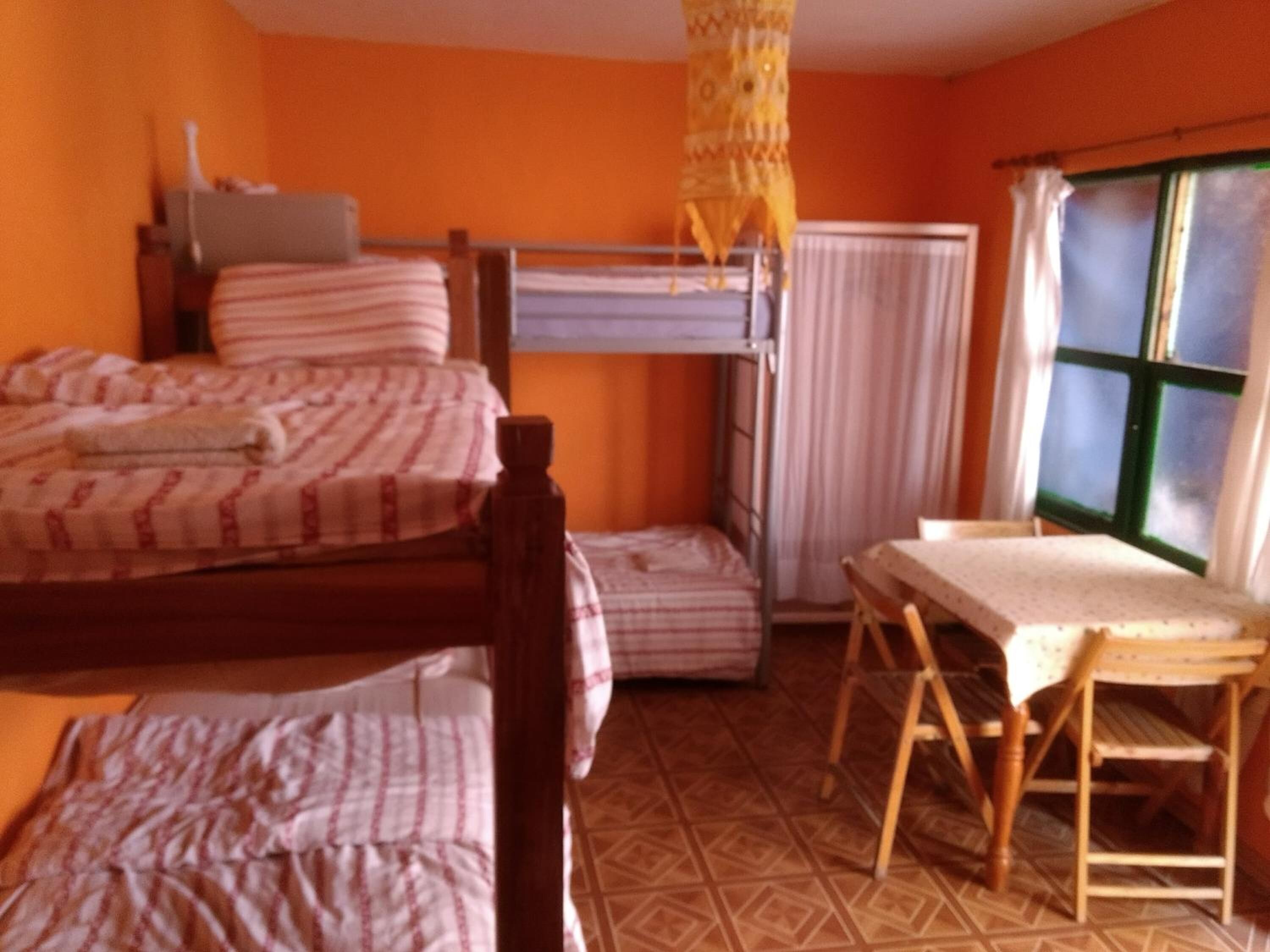 A dormitory room with two bunk beds, a wooden chair, a table, and a window with curtains.