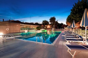 Une piscine entourée de bâtiments et d’arbres, avec des chaises longues et des parasols.