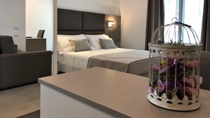 Moderni hotellihuone, jossa on sänky, työpöytä ja koristeellinen lasinen lintuhäkki, jossa on kukkia.