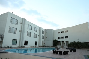 A modern building with a swimming pool and outdoor seating area. - Neel's City Resort (Rajkot)