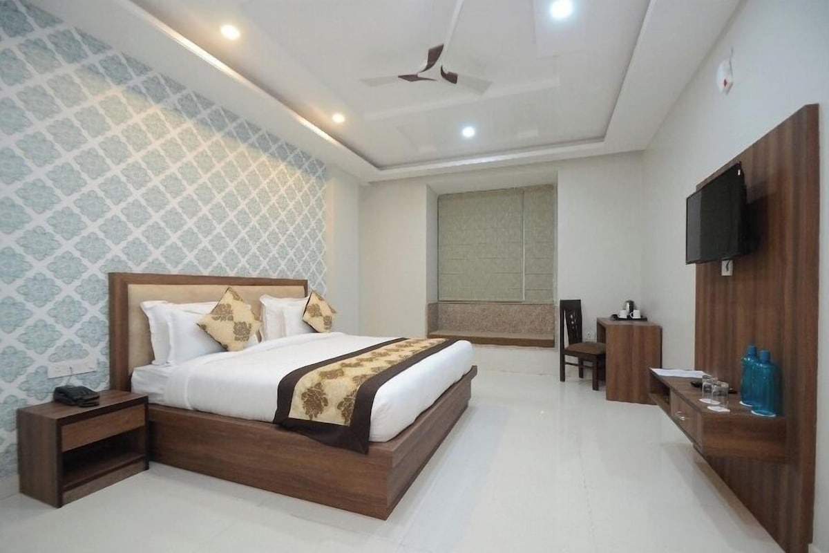 A hotel room with a bed, bedside table, TV, and a desk with a chair.