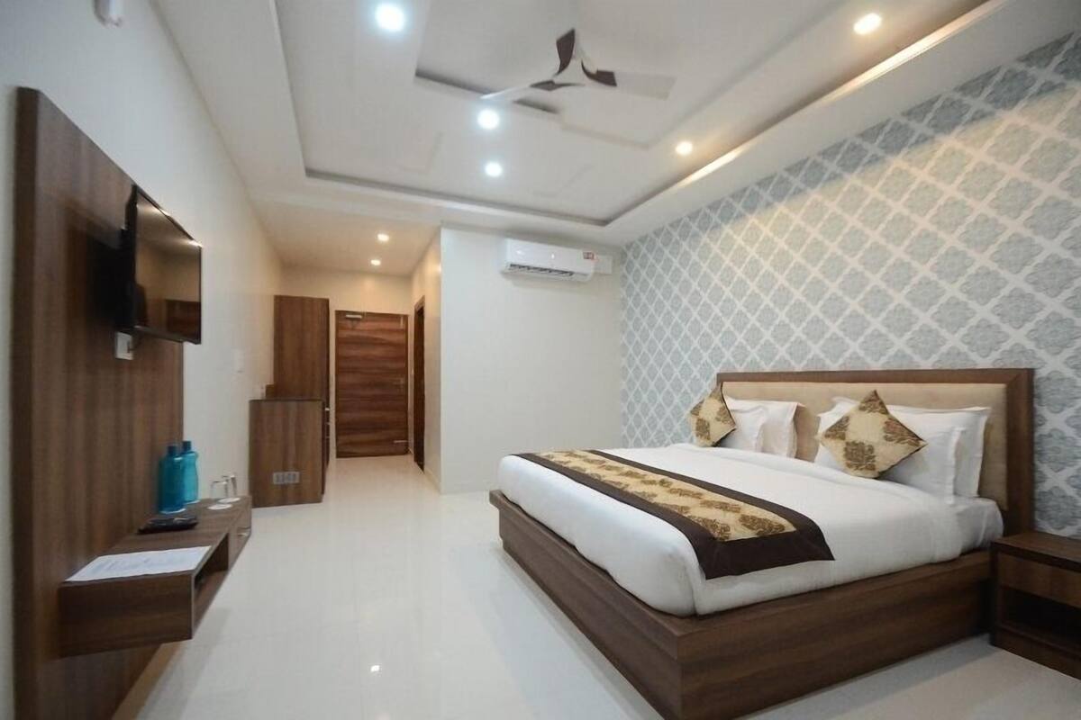 Una habitación de hotel moderna con una cama grande, cabecera de madera, un televisor de pantalla plana montado en la pared, un ventilador de techo y un papel tapiz estampado.