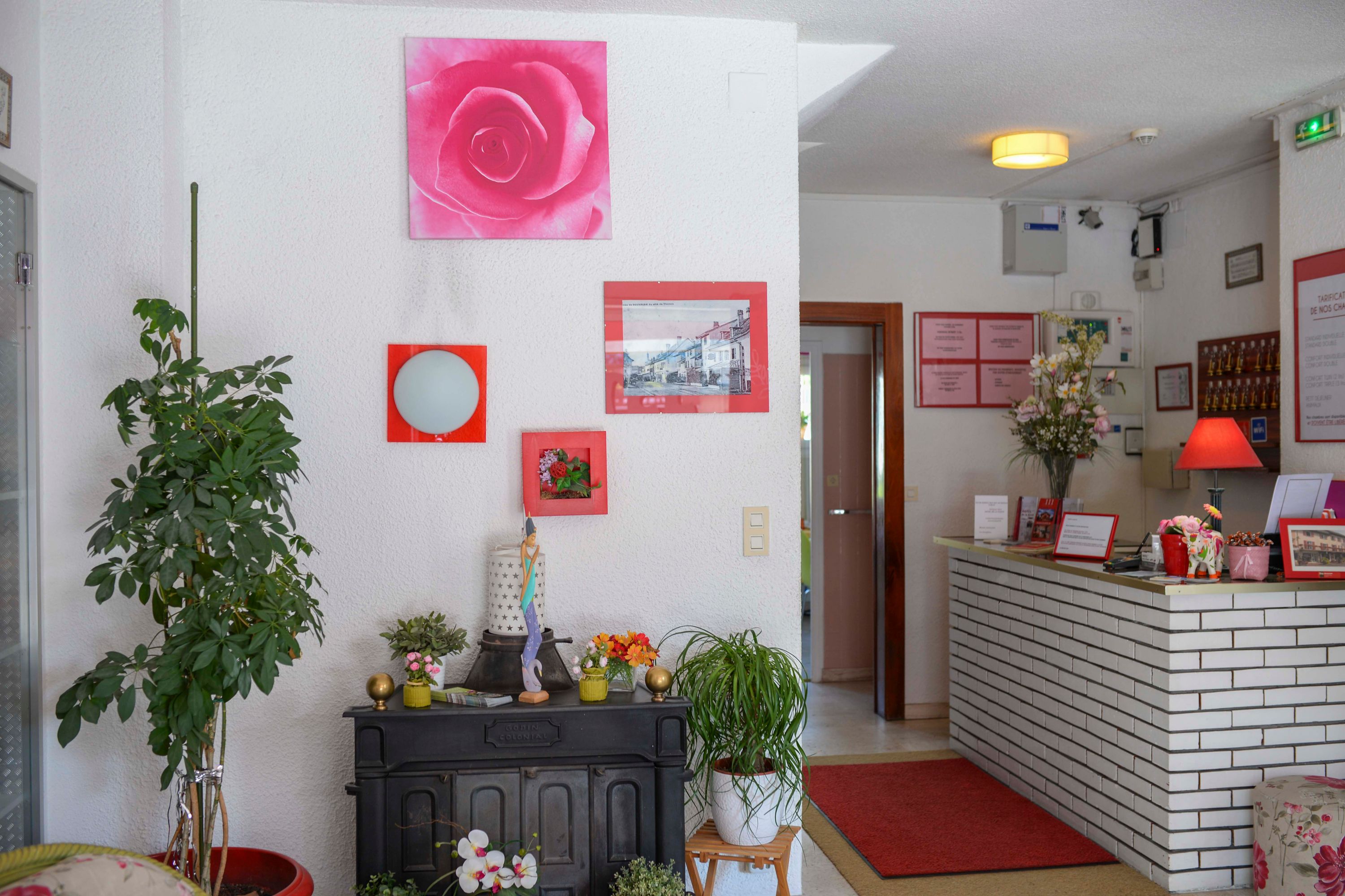 Un área de recepción con mostrador de ladrillo, plantas en macetas e imágenes enmarcadas en la pared.