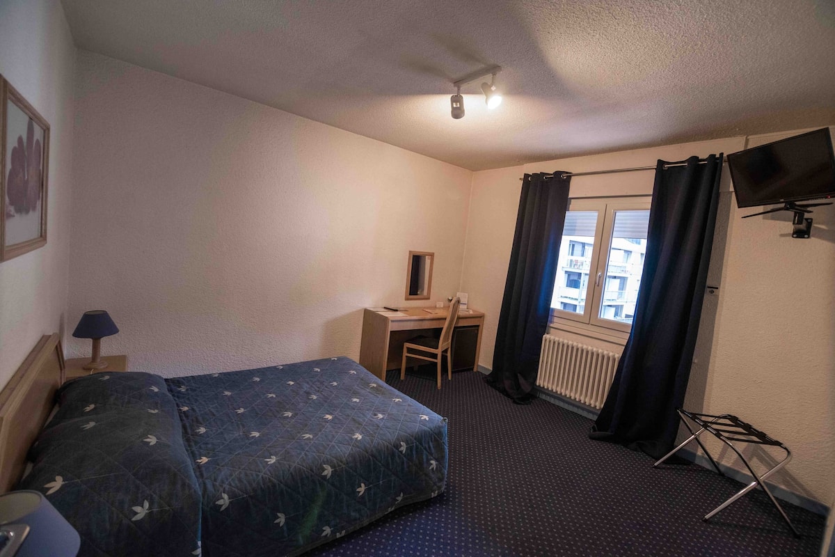 A hotel room with a bed, desk, chair, and a TV mounted on the wall.