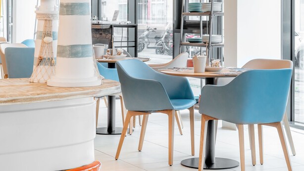 A modern dining area with a lighthouse centerpiece, blue chairs, and large windows. - myNext - Hotel Leo (Vienna)