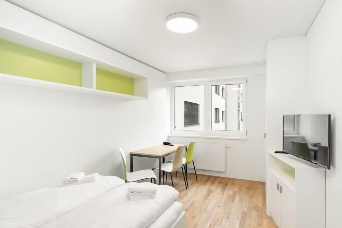 A modern, compact room with a bed, a desk, and a television.