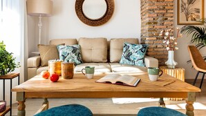 Ein gemütliches Wohnzimmer mit Backsteinwand, einem runden Spiegel, einem Holztisch und einer Couch mit gemusterten Kissen.