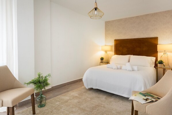 A hotel room with a bed, two bedside tables with lamps, a chair, a small plant, and a hanging light fixture. - Genteel Home Plaza de las Flores (Malaga)