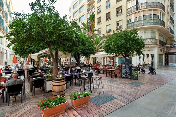 Un área de café al aire libre con mesas y sillas, rodeada de árboles y edificios.