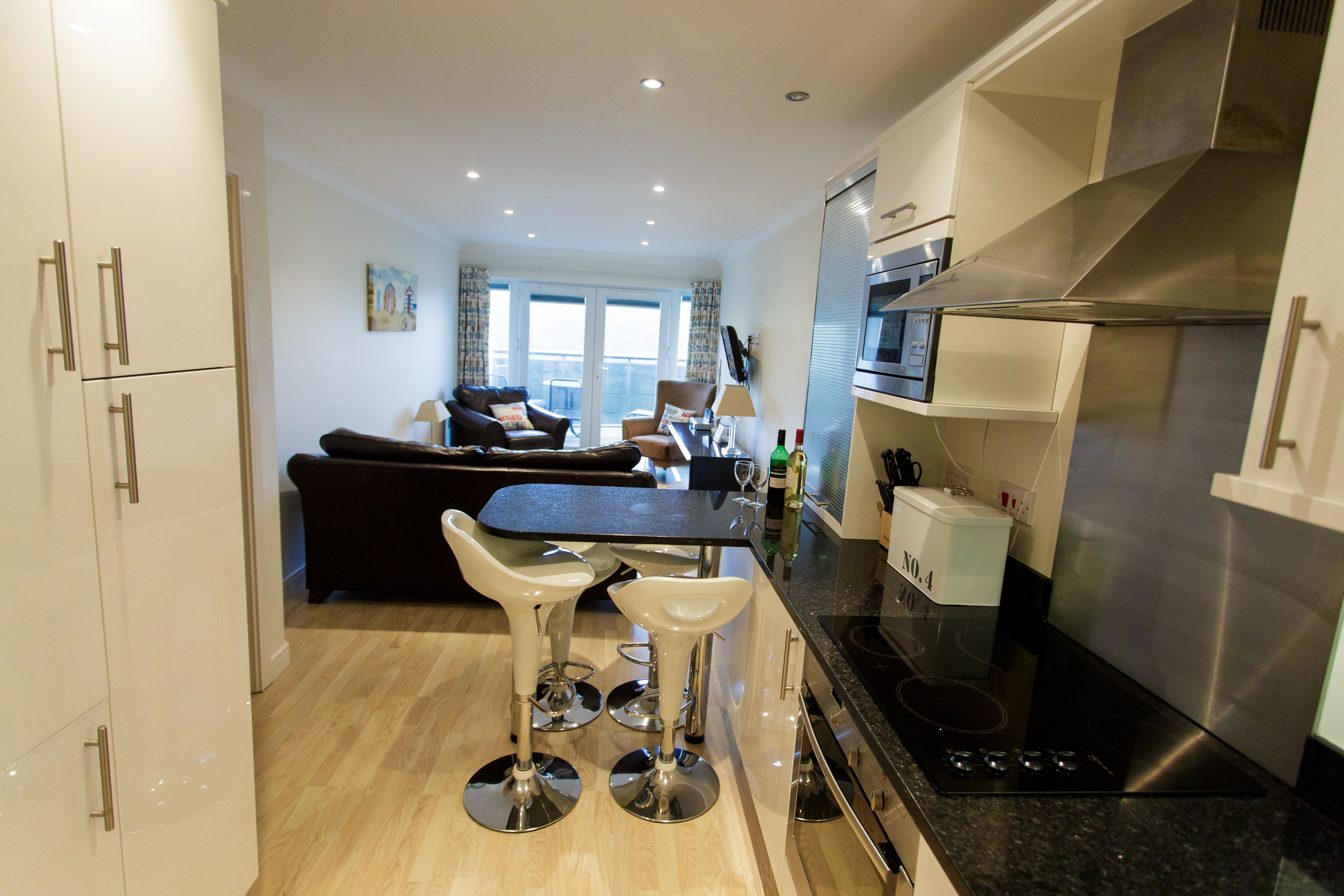 A modern kitchen with a black countertop, stainless steel appliances, and a dining area with two bar stools.