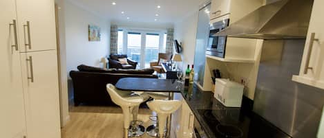 A modern kitchen with a black countertop, stainless steel appliances, and a dining area with two bar stools.