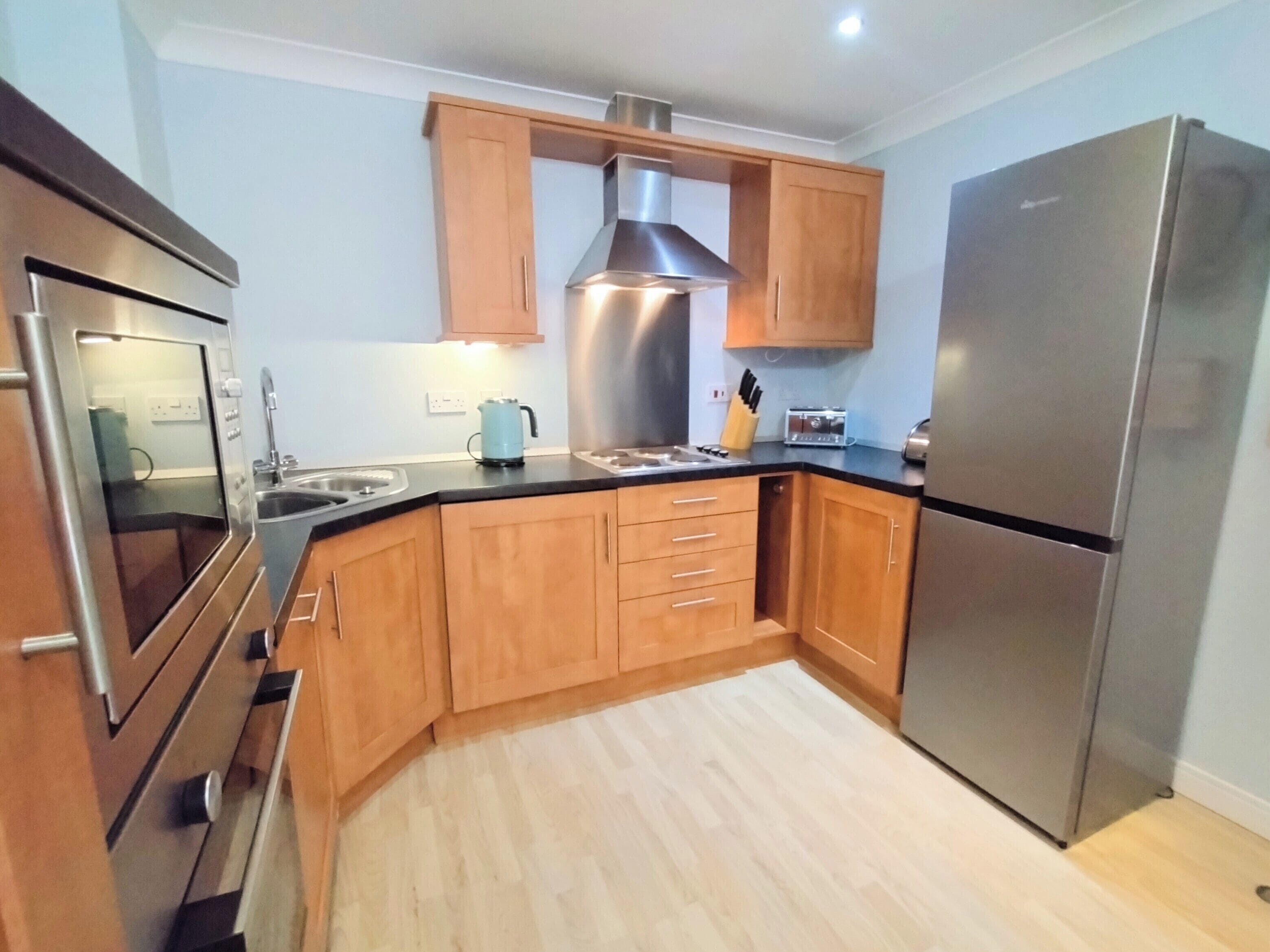 Une cuisine moderne avec des meubles en bois, des appareils électroménagers en acier inoxydable et un plancher en bois clair.