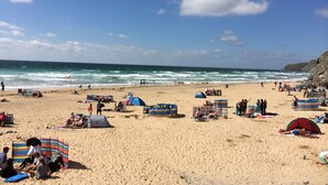 A beach with tents, umbrellas, and people. - Waves Apartments (Newquay)