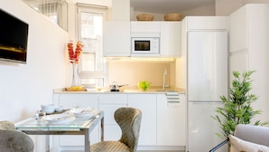 Una cocina moderna con armarios blancos, microondas, refrigerador y un comedor con mesa y sillas de vidrio.