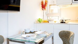 Una cocina moderna con armarios blancos, una mesa de vidrio y dos sillas tapizadas.