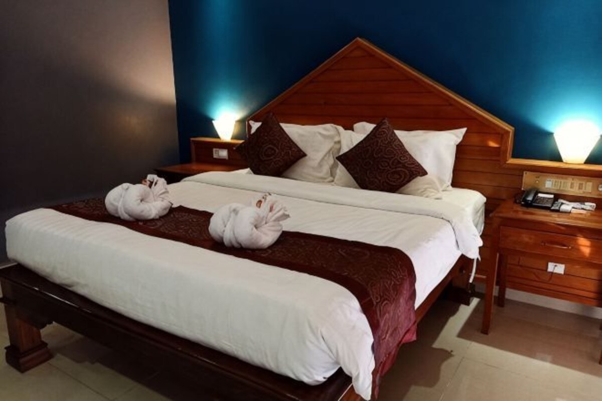 Una cama bien tendida con sábanas blancas, cabecera de madera y dos mesitas de noche con lámparas.