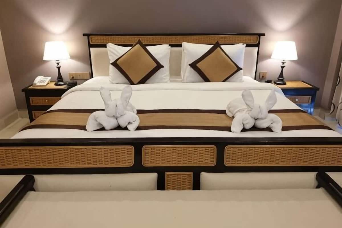 Une chambre d’hôtel avec un grand lit, deux tables de chevet, une lampe de chaque côté et une serviette décorative disposée sur le lit.