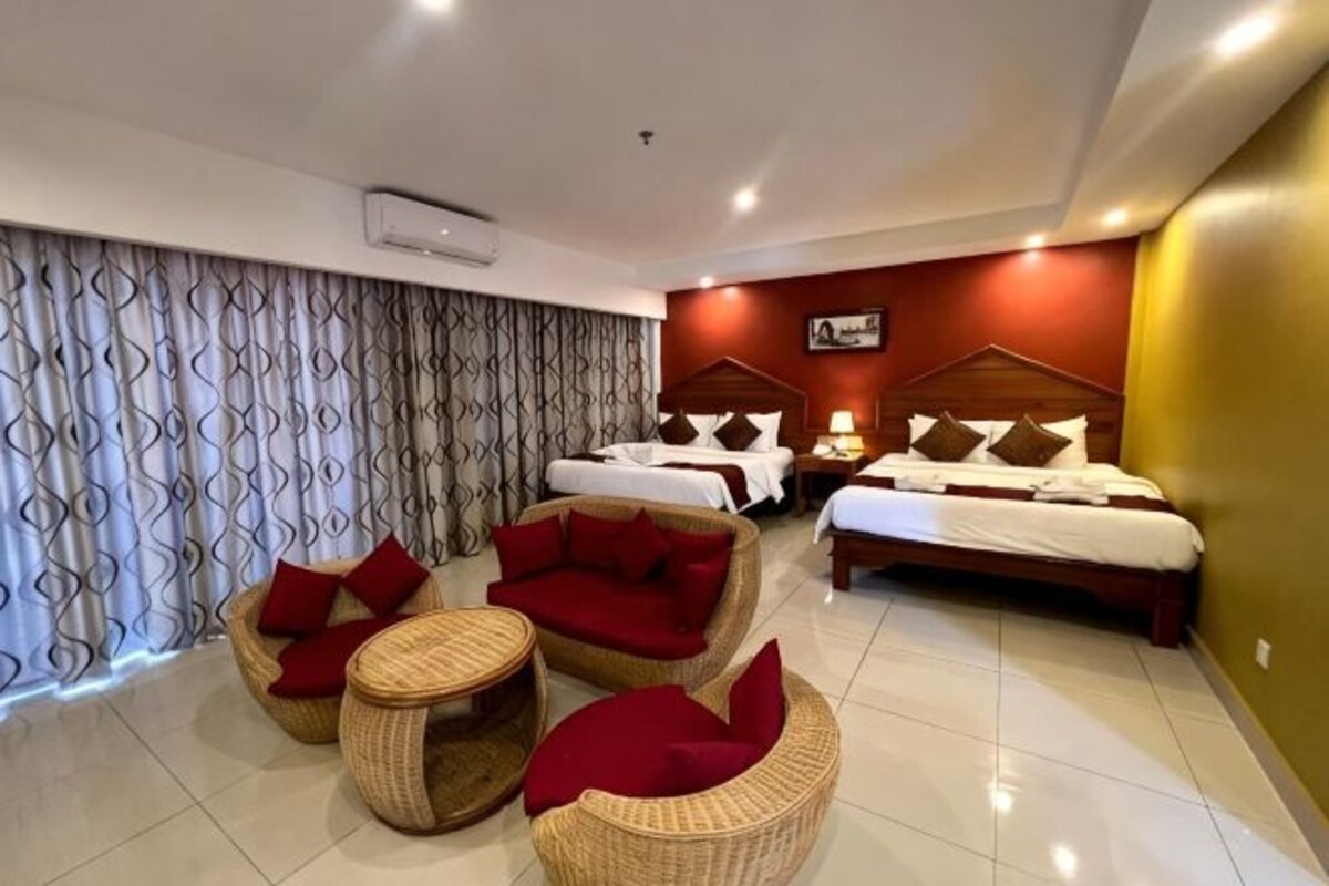 Una habitación de hotel con una cama, dos sofás rojos, una mesita y un ventanal con cortinas.