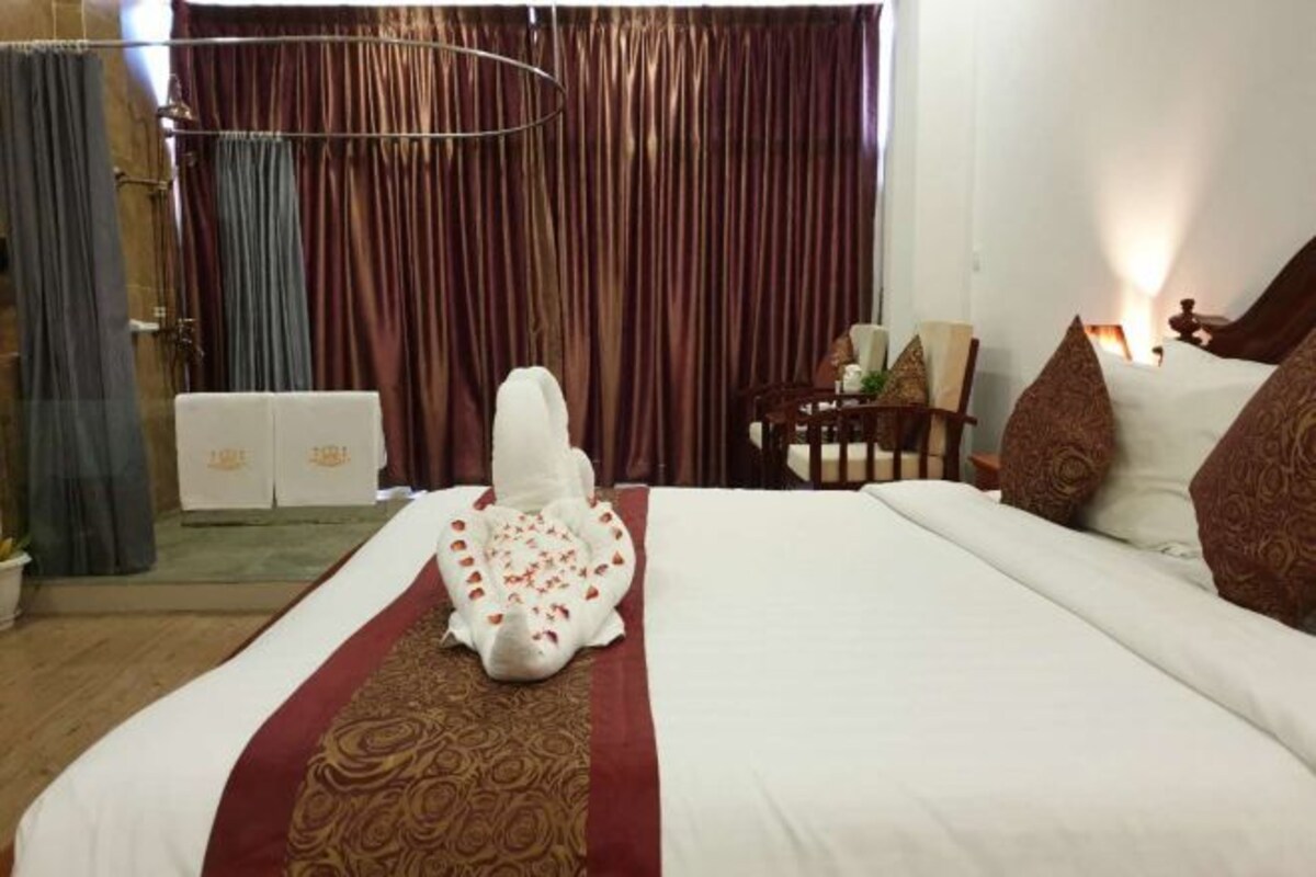 Una habitación de hotel con una cama grande, una silla, una mesa y un cortinero.
