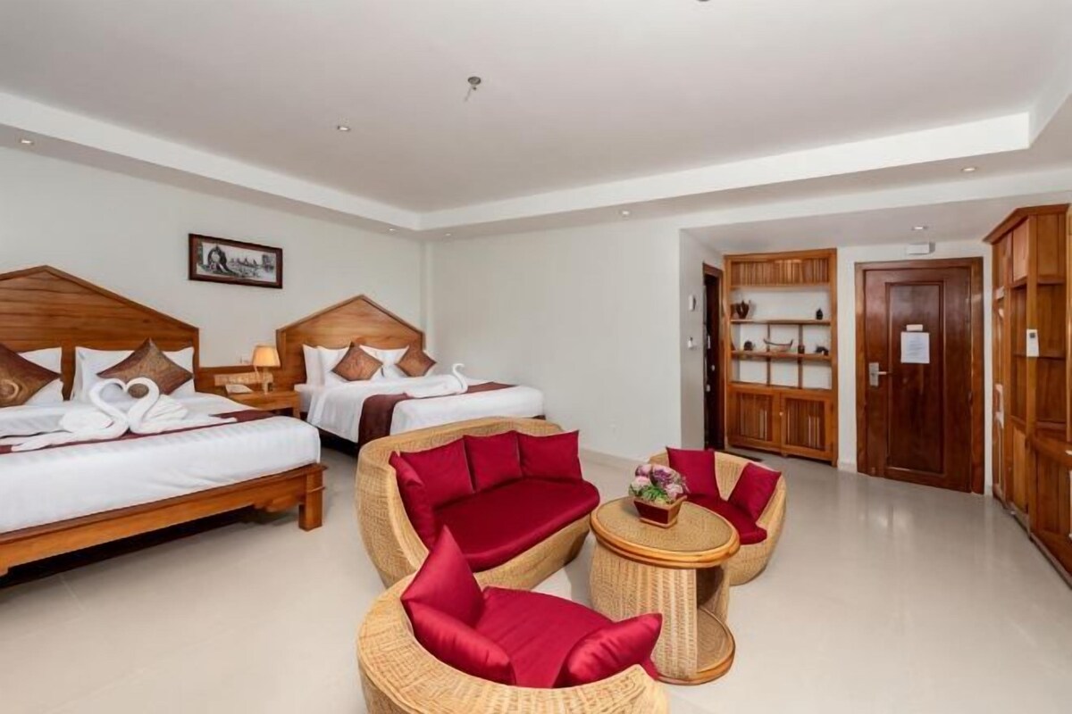 Habitación de hotel con dos camas, zona de estar con muebles de mimbre y armarios de madera.