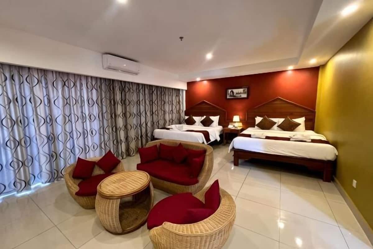 Une chambre d’hôtel avec un lit, deux canapés rouges, une petite table et une grande fenêtre avec des rideaux.