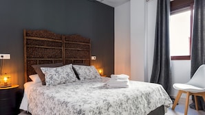 Ein Schlafzimmer mit einem Bett, einem Nachttisch, einer Lampe, einem Sessel und einem Fenster.