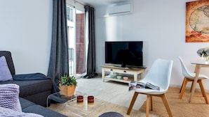Ein modernes Wohnzimmer mit einer Couch, einem Couchtisch mit Pflanze, einem Fernseher und einem Essbereich mit Stühlen.