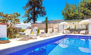 Una piscina con sillas de descanso y sombrillas, rodeada de árboles y un edificio.