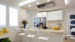 Une cuisine moderne avec des meubles blancs, un réfrigérateur en acier inoxydable et un coin bar avec des chaises blanches.