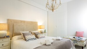 Une chambre à coucher avec un grand lit, des tables de chevet, une commode, un petit tabouret et un lustre.