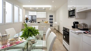 Une cuisine moderne avec des meubles blancs, un four en acier inoxydable et un four à micro-ondes. On y trouve également un coin repas avec une table en verre et des chaises blanches.