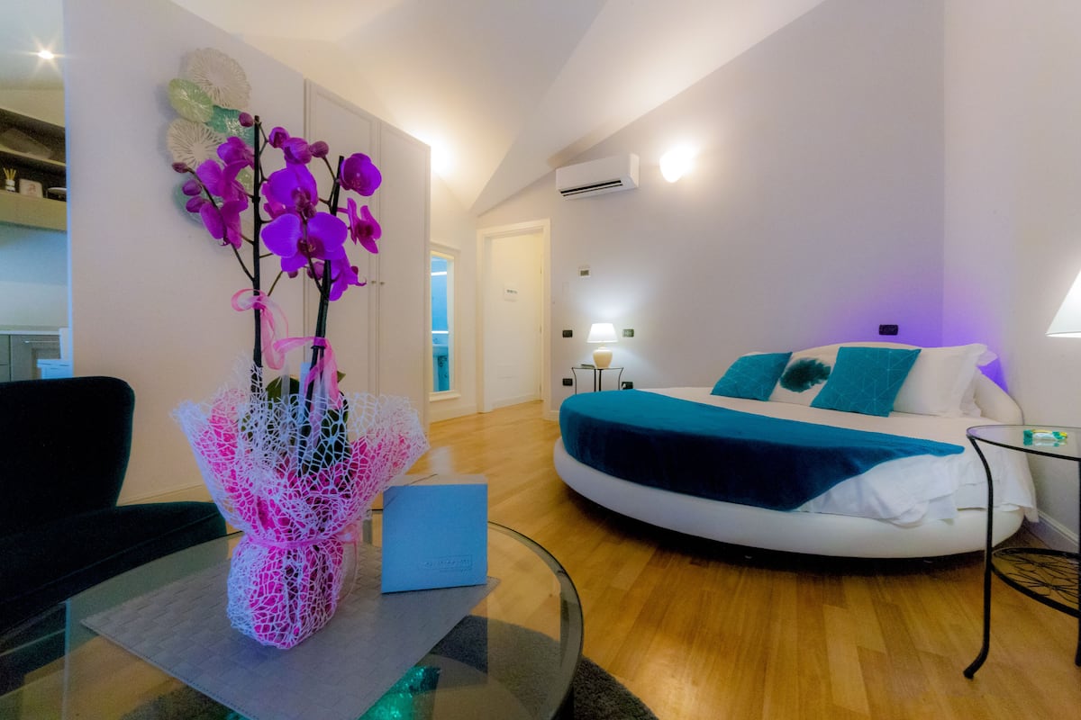 A modern bedroom with a curved bed, a glass coffee table, and a vase of purple orchids.