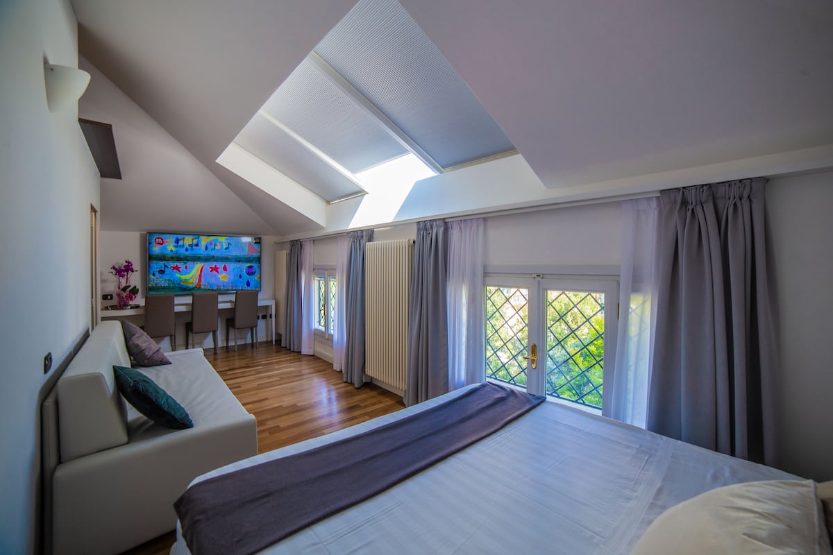 A bedroom with a large bed, a sofa, a TV, and a desk area.