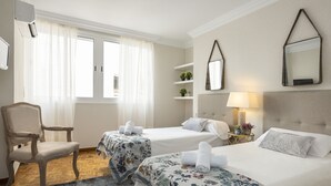 A hotel room with two beds, a chair, a small table with a lamp, and a window with curtains. - Genteel Home Tomas Heredia (Malaga)