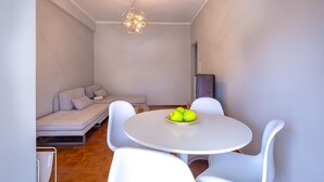 A modern dining area with a round table and white chairs, a sofa, and a ceiling light fixture. - Artemis Deluxe Athens City Center Apartment (Athens)