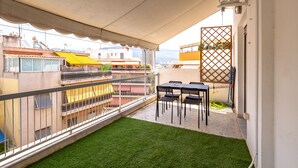 A balcony with a small grassy area, a table with chairs, and a view of neighboring buildings. - Artemis Deluxe Athens City Center Apartment (Athens)