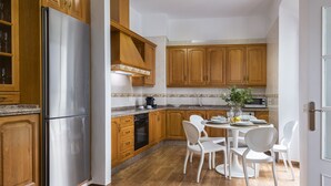 Une cuisine avec des meubles en bois, un réfrigérateur en acier inoxydable, un four à micro-ondes et une table à manger avec des chaises blanches.