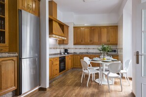 Una cocina con armarios de madera, un refrigerador de acero inoxidable, un microondas y una mesa de comedor con sillas blancas.