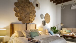 Une chambre bien éclairée, avec un grand lit, une table de chevet, une lampe de lecture et un mur décoré de paniers tressés.