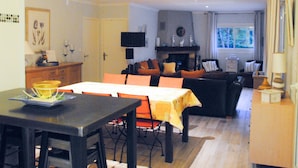 A dining area with a table and chairs, a sofa, and a fireplace in the background.