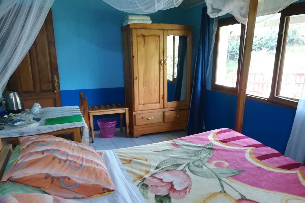 Ein Schlafzimmer mit einem Bett, einem Holzschrank, einem kleinen Tisch mit Stuhl und einem Fenster mit Vorhängen.