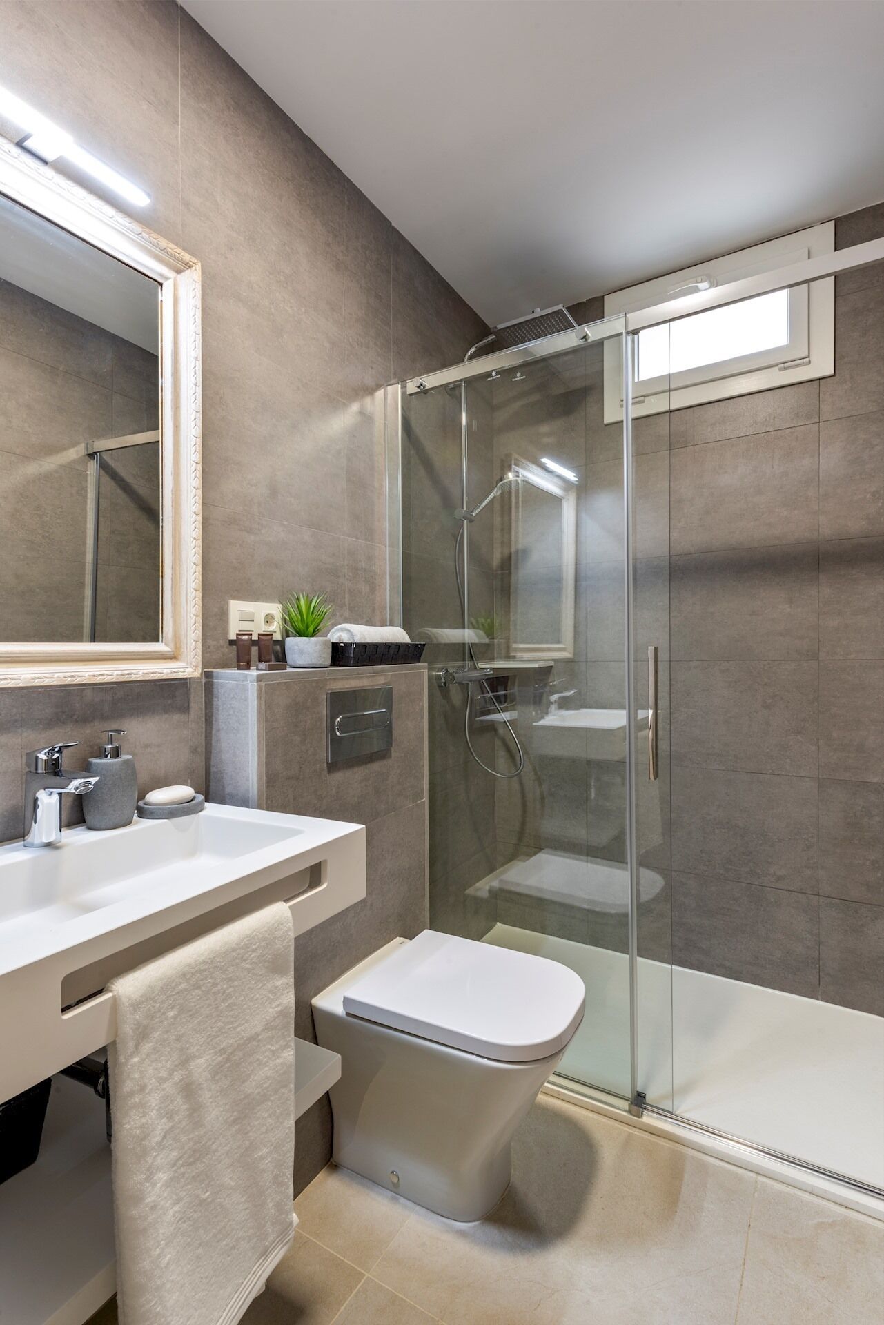Un baño moderno con ducha envuelta en vidrio, inodoro blanco y tocador con espejo y lavamanos.