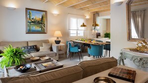 Ein modernes Wohnzimmer mit einer Couch, einem Couchtisch mit Büchern und Dekoration, einer Essecke mit blauen Stühlen und einer Küche mit Esstisch.
