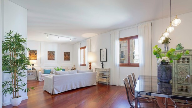 Ein geräumiges Zimmer mit einem Bett, einem Esstisch mit Stühlen, einer Topfpflanze und Bildern an den Wänden.
