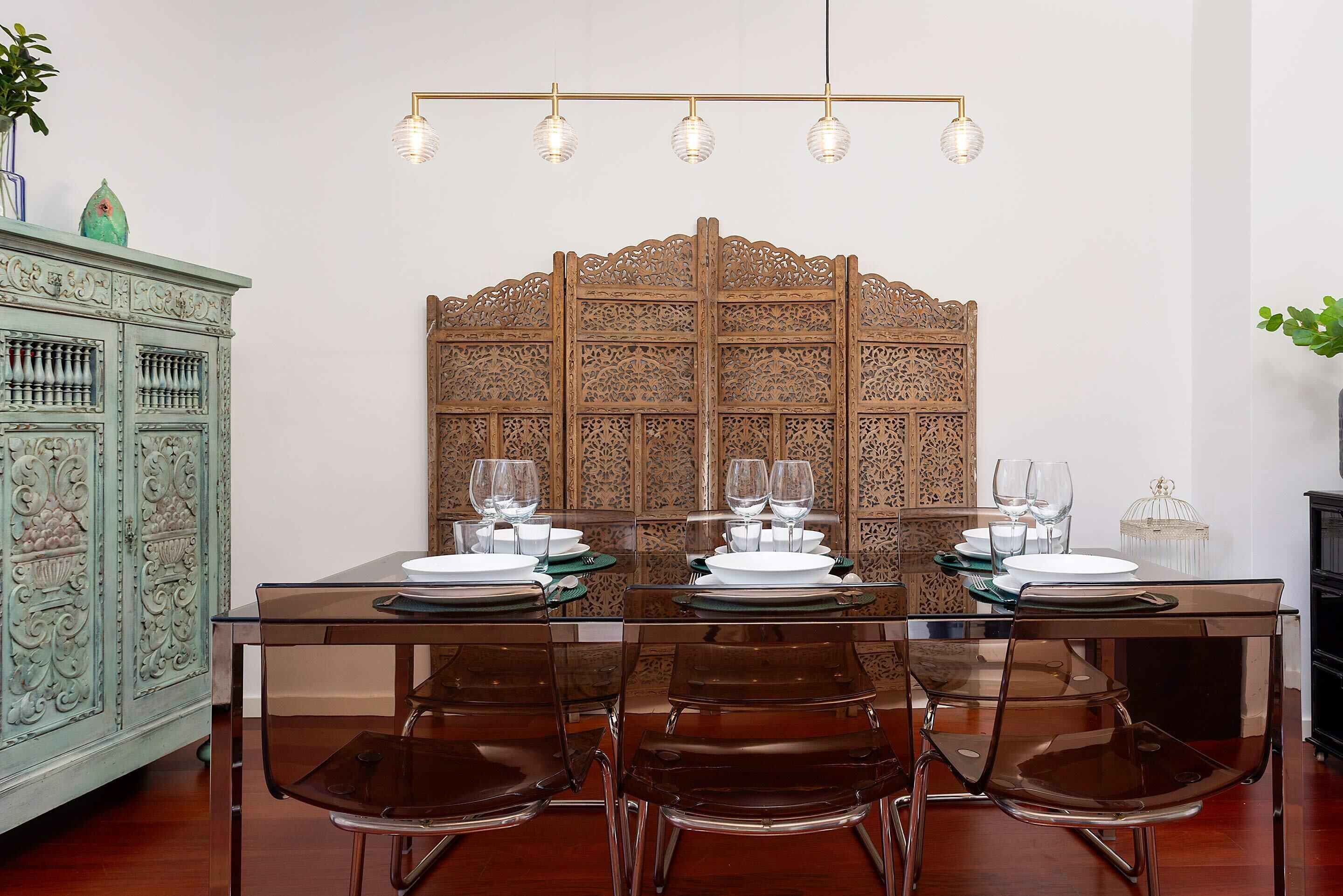 Een eetruimte met een houten scheidingswand, een glazen tafel en bruine stoelen.