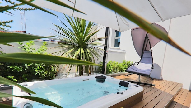 Een hottub op een houten terras, met een hangstoel en een plant in pot op de voorgrond.