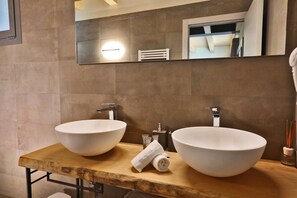 Un baño con dos lavamanos blancos de pedestal, un mueble de tocador de madera, un espejo y una toalla.
