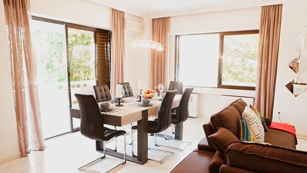 A modern dining area with a table set for four, surrounded by chairs, and a brown sofa with cushions. - Glyfada Center - Aries Newly Modern Home (Glyfada)