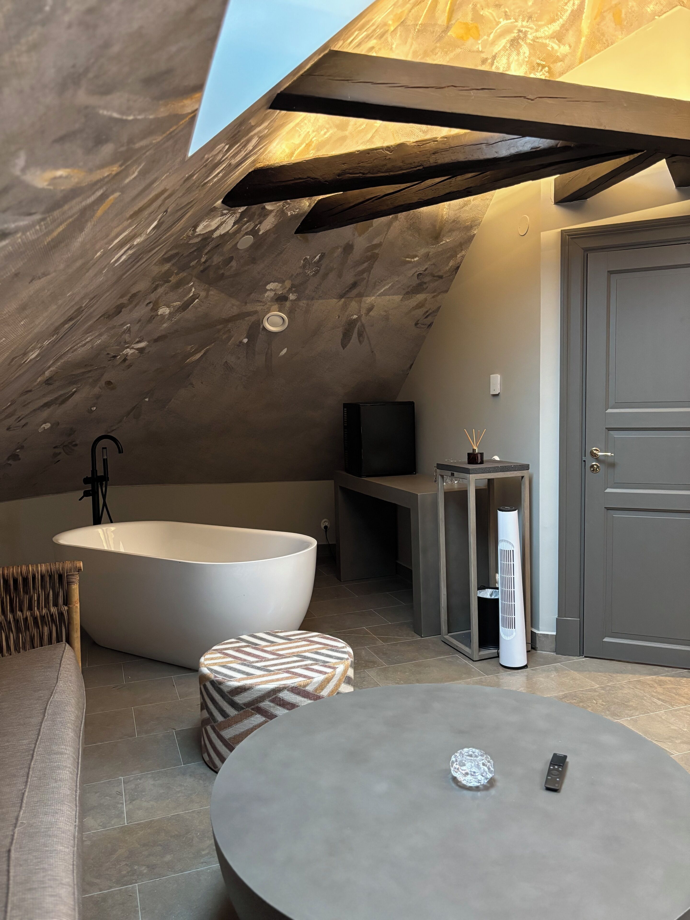 Une chambre aménagée dans les combles, avec une grande baignoire, une télévision, une petite table et une porte.